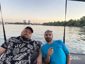 Two friends relax on a boat, enjoying the serene waters and city skyline in the background — perfect for a laid-back day on the water.