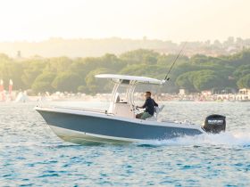 A man navigates a speedboat through shimmering waters, perfect for fishing adventures or leisurely outings on the coast.