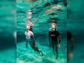 Two friends enjoy a refreshing swim underwater in crystal-clear waters, capturing the essence of fun and adventure in tropical destinations.