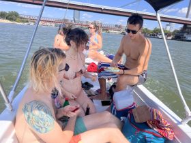A lively group enjoys a sunny day on the water, sharing food and drinks aboard a boat — perfect for summer gatherings and celebrations.
