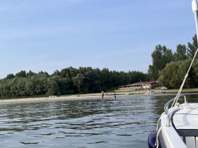 A group enjoys a sunny day at the beach, with children playing in the water and a boat anchored nearby — a perfect summer getaway.