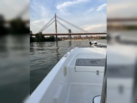 A view of a sleek boat navigating the water, showcasing the hull and the backdrop of a striking bridge and city skyline.