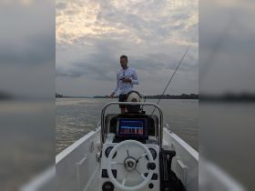 A man stands on a fishing boat, actively engaged in his activity on the water, showcasing the thrill of fishing adventures.