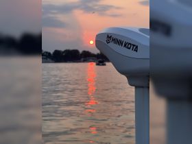A serene sunset view featuring the Minn Kota motor of a boat, reflecting vibrant colors on the water's surface — perfect for capturing tranquil moments on the water.