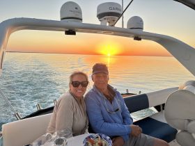 A couple enjoys a romantic sunset on a boat, capturing the perfect moment against a stunning backdrop of vibrant colors on the water.