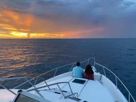 A couple enjoys a romantic sunset view from the bow of a boat, creating a perfect backdrop for memorable moments on the water.