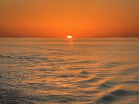 A stunning sunset casts a warm glow over calm waters, creating a picturesque scene perfect for romantic evenings or serene boat rides.