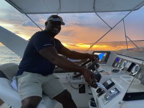 A smiling captain steers the boat into a stunning sunset, showcasing the perfect blend of adventure and natural beauty on the water.