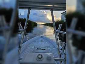 A captivating view from the front of a Lake & Bay boat, gliding through calm waters with a stunning sunset backdrop — perfect for serene boating adventures.