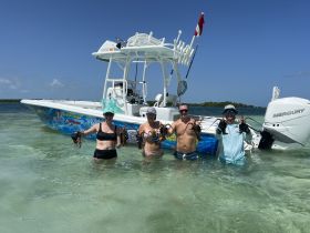 A group of friends celebrates their successful lobster catch while wading in shallow waters next to their boat — a perfect day of fishing and fun in the sun.