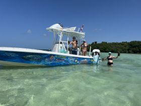 A group of friends celebrates their catch while wading in shallow waters next to a boat, showcasing a fun day of lobster hunting in a tropical paradise.