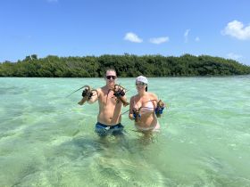 A couple proudly displays their catch of lobsters while wading in the crystal-clear waters, showcasing a fun snorkeling adventure in a tropical paradise.