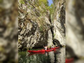 Two kayakers navigate through a stunning canyon, surrounded by towering cliffs and lush greenery — an ideal setting for adventure and exploration.