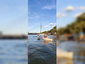 Two kayakers paddle through serene waters with a stunning bridge in the background, capturing the essence of outdoor adventure and scenic exploration.