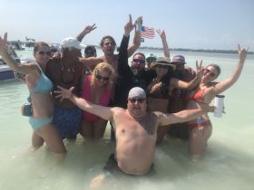 A lively group of friends celebrates in shallow waters, enjoying a fun day at the beach with drinks and laughter — perfect for unforgettable summer memories.