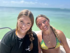Two friends smile brightly for the camera while enjoying a sunny day by the water, capturing the essence of fun and friendship on a boating adventure.
