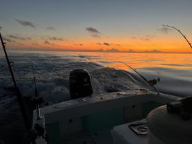 A serene sunset view from a fishing boat, showcasing the tranquil ocean waters and the silhouette of fishing rods, perfect for capturing the essence of a peaceful evening on the water.