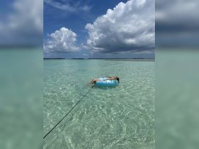 A person relaxes on a floating tube in crystal clear waters, enjoying a serene day under the clouds — a perfect snapshot of summer fun and relaxation.