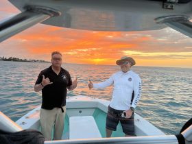 Two friends enjoy a stunning sunset on the water, capturing the perfect moment of camaraderie and celebration aboard their boat.