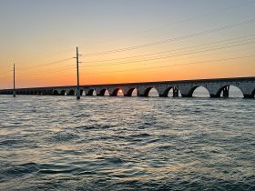 A stunning sunset view behind a historic bridge, reflecting beautifully on the water — a perfect backdrop for evening boat trips.