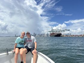 A happy couple poses for a photo on their boat with a stunning city skyline in the background, capturing a perfect day on the water.