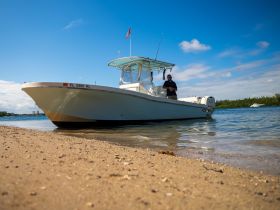A man stands next to a boat on the beach, showcasing a perfect day for boating adventures in clear waters.