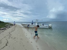 A group of people, including children, enjoy a beach day with a boat anchored nearby, creating a perfect setting for family fun and water activities.