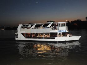 The Sirena boat glides through the water at dusk, filled with guests enjoying a lively dinner cruise — perfect for celebrations and social gatherings on the water.