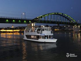 A scenic view of the Sirena boat cruising on the river at night, illuminated by city lights and a striking bridge, perfect for evening river cruises.