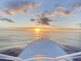A serene sunset view from the bow of a boat, showcasing calm waters and a vibrant sky — perfect for peaceful evening cruises.