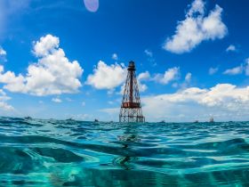 A stunning view of a lighthouse rising above the turquoise waters, surrounded by boats under a bright blue sky — a perfect representation of coastal beauty.