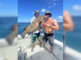 Two anglers proudly display their impressive catch while fishing on a boat, showcasing the thrill of a successful day on the water.