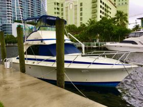 A well-maintained yacht docked at a marina, showcasing its sleek design against a backdrop of modern buildings and lush greenery.