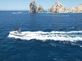 A sleek speedboat navigates the vibrant waters near the iconic rock formations of Cabo San Lucas, showcasing the beauty of marine adventures.