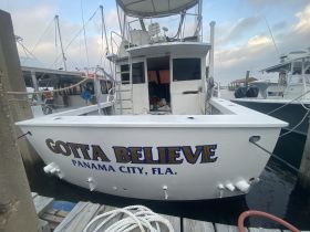 The 'Gotta Believe' boat is docked in Panama City, showcasing its distinctive name and structure against a serene marina backdrop.