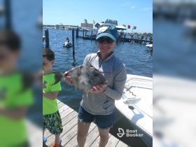 A joyful moment as a woman proudly holds her catch of the day, a fish, while a child stands beside her at the dock — perfect for family fishing adventures.