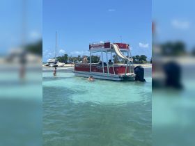 A lively group enjoys a sandbar stop aboard a party pontoon, with guests swimming and relaxing in the shallow waters — perfect for summer fun and group outings.