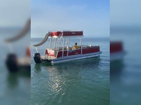 A vibrant red pontoon boat is docked on calm waters, showcasing its fun slide and spacious seating — perfect for family outings or leisurely cruises.