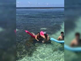 A group of friends enjoys a refreshing swim in crystal-clear waters, relaxing on floating mats — a perfect day for fun and relaxation under the sun.