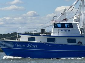 A striking blue fishing boat named 'Jesus Lives' navigates through calm waters, showcasing its unique design and purpose.
