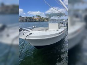 A clear view of a center console boat docked in calm waters, showcasing its sleek design against a backdrop of palm trees and waterfront homes.