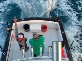 A group of friends enjoys a fishing trip on a boat, capturing the excitement of the ocean experience with fishing rods at the ready.