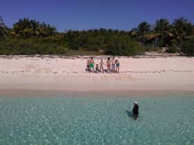 A lively group enjoys a beach day in Cozumel, capturing memories with a sandy greeting and fun in the clear waters.