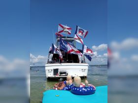 A lively scene featuring a man relaxing on a floating mat with inflatable figures while enjoying drinks near a decorated boat — perfect for summer parties and celebrations on the water.