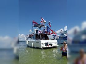 A festive boat adorned with flags is anchored in shallow waters, with guests enjoying the sun and water — perfect for summer celebrations on the water.