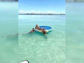 A lively group of friends enjoys a sunny day floating on a mat in crystal-clear waters, perfect for relaxation and fun in the sun.