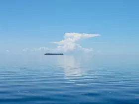 A serene view of a tranquil sea with a distant island and reflective clouds, perfect for showcasing the beauty of coastal destinations.