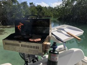 A close-up of a grill on a boat, cooking burgers amidst a scenic mangrove backdrop — perfect for onboard barbecues and outdoor dining experiences.