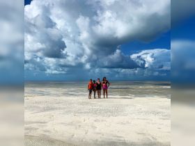 A joyful group stands on a sandbar, surrounded by shallow waters and dramatic clouds — a perfect moment capturing the essence of a beach adventure.