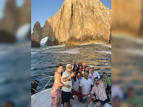 A lively group poses on a boat near the iconic rock formation in Cabo San Lucas, capturing the essence of a fun-filled day on the water.